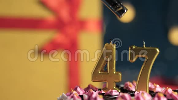 生日蛋糕编号47金色蜡烛用打火机点燃蓝色背景礼品黄色盒子用红丝带系好视频的预览图