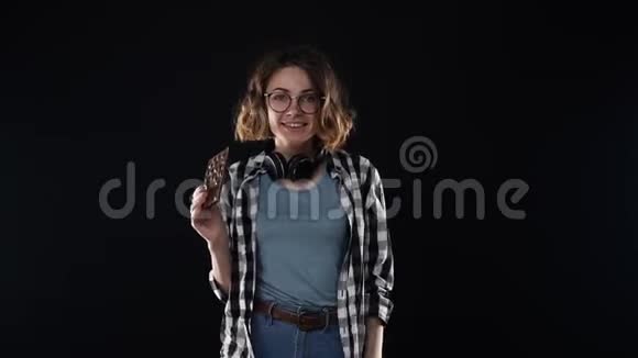 穿着格子衬衫和牛仔裤的美丽黑发年轻女子微笑着摆着姿势吃着手里拿着的巧克力棒和坚果隔离开来视频的预览图