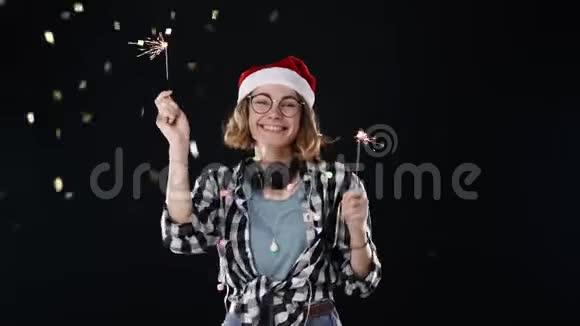 一位戴着圣诞帽位戴着圣诞帽戴着五颜六色的花环戴着耳机的可爱女子在圣诞夜舞会上翩翩起舞视频的预览图