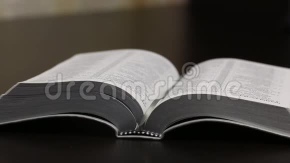 桌子上放着一本公开的圣经一个人读它移动他的手指沿着线条翻页特写镜头视频的预览图