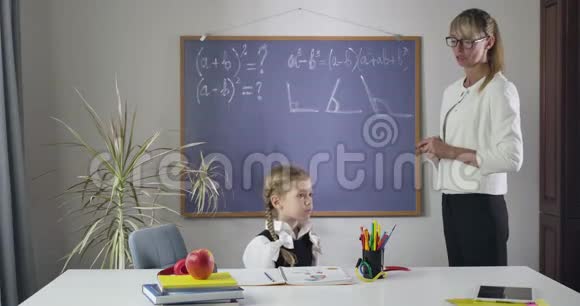 疲惫的白种人中年家庭教师用手抱着头像坐在桌子旁的可爱女学生一样大喊大叫教师视频的预览图