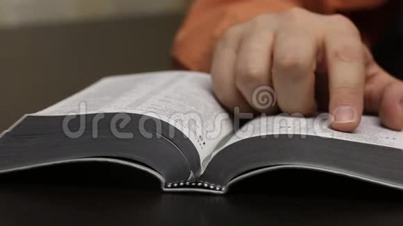 桌子上放着一本公开的圣经一个人读它移动他的手指沿着线条翻页撕下书签关闭视频的预览图