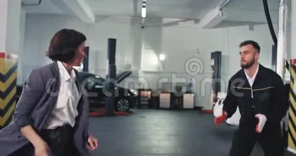漂亮的经理女人穿着西装机械师男人在车库里跳舞当他们完成后他们看起来很迷人视频的预览图