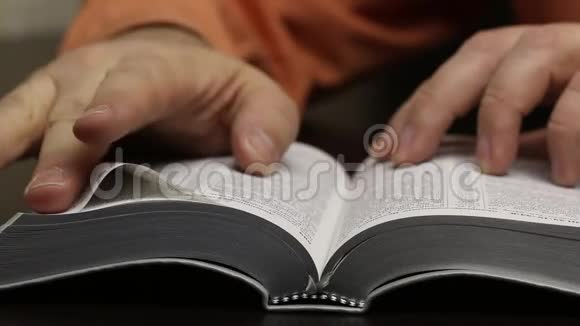 桌子上放着一本公开的圣经这个人迅速翻页寻找想要的章节阅读引导手指沿着视频的预览图