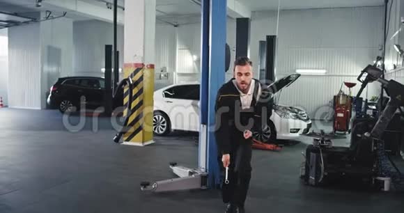 一个身穿制服的机械师在一个大型的汽车服务中心跳着滑稽的舞蹈他在工作中有着很好的心情热爱他的工作视频的预览图