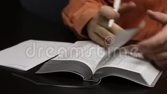 一个人坐在桌边读圣经把重要的思想写在一张纸上撕下书签关闭视频的预览图