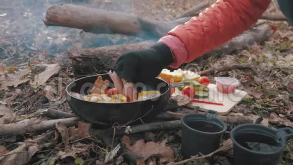 远足时在篝火上做饭一个女孩在篝火上用平底锅准备鸡蛋和西红柿和培根在露营视频的预览图