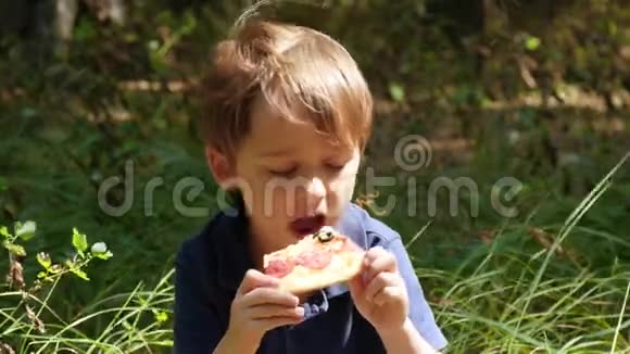 可爱的白种人男孩在公园里吃一片比萨饼视频的预览图