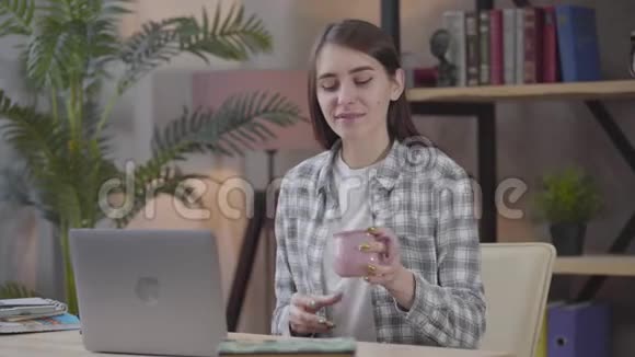 自信的白种人黑发女人的肖像她把茶或咖啡切在桌子上在笔记本电脑键盘上打字视频的预览图