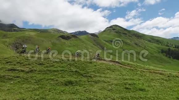 下坡自行车鸟瞰一群山地自行车手在绿色的山顶上追踪视频的预览图