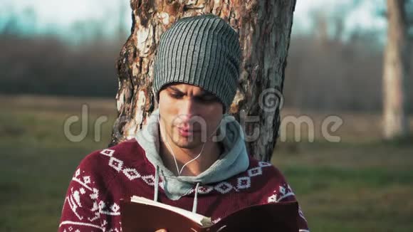 年轻的白种人男孩坐在树附近的中田里读着一本关于自然和森林背景的书秋天近点视频的预览图