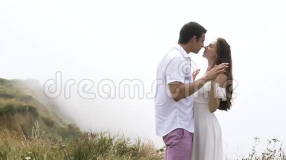 年轻夫妇拥抱在悬崖边背景上有浓雾行动温柔的男人和女人享受视频的预览图