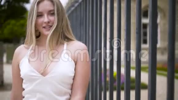 年轻的金发女人户外肖像行动迷人的性感女孩长发慢慢地沿着铁栅栏走着视频的预览图