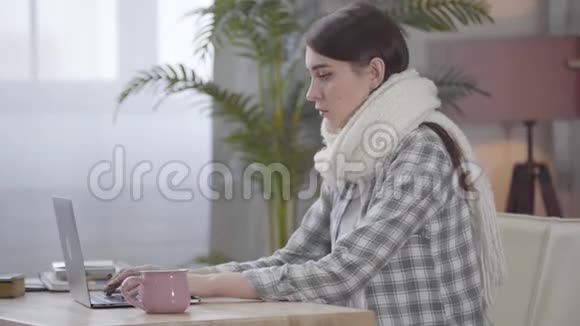 白人女孩戴着白色围巾在笔记本电脑键盘上打字咳嗽我的自由职业者视频的预览图