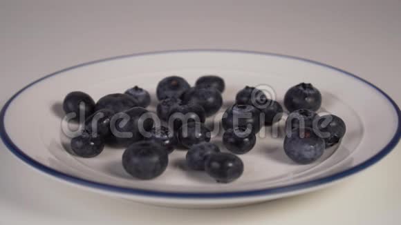 蓝边框的白色盘子上的蓝莓白色酸奶落在浆果上视频的预览图
