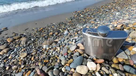 海滩上鹅卵石上的老式金属臀部烧瓶庆祝人们海上度假视频的预览图