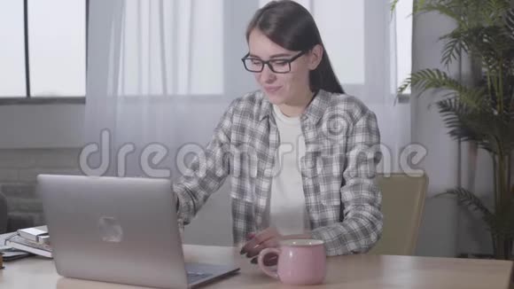 可爱的白种人黑发女孩戴着优雅的眼镜在笔记本电脑键盘上打字自信微笑的女性自由职业者视频的预览图