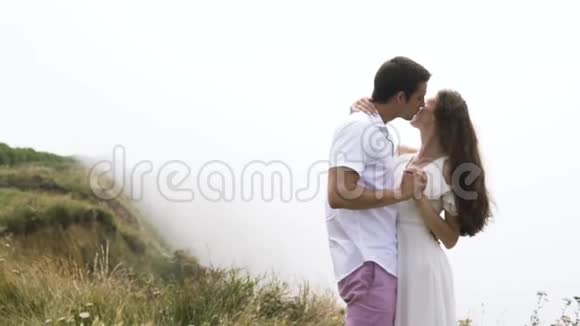 年轻夫妇拥抱在悬崖边背景上有浓雾行动温柔的男人和女人享受视频的预览图