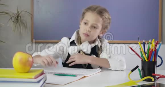 迷人的白人女学生在练习本上写字咬着苹果伸出大拇指快乐女生做视频的预览图