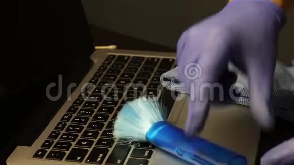 一个男人用刷子清除笔记本电脑键盘上的灰尘他拿着棉签用清洁剂蘸着带棉花的洁面乳视频的预览图