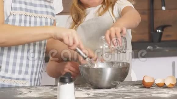 母亲和女儿的特写双手在金属碗里搅拌面团视频的预览图