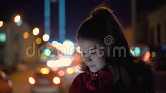 年轻漂亮的女人看着电话在夜城的街道上微笑着视频的预览图