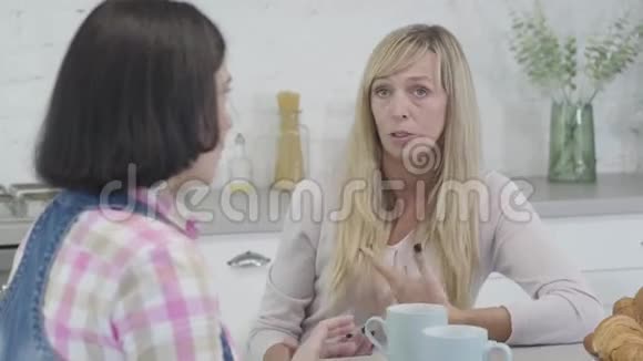 成年金发白种人妇女与黑发女性朋友交谈和手势的肖像女人闲谈就像坐在视频的预览图
