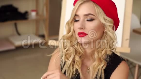 一个金发女郎的特写她的妆容鲜艳红唇坐在艺术工作室里视频的预览图