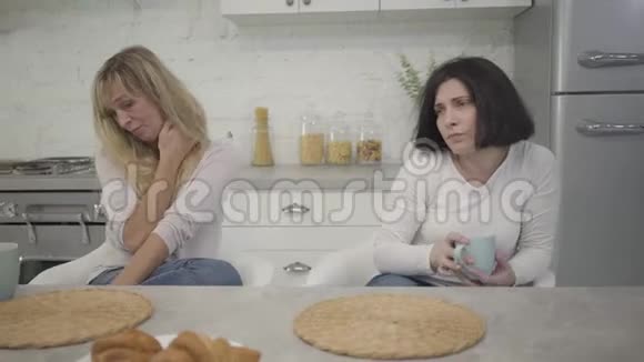 镜头围绕着两个白人成年妇女坐在桌前喝咖啡精疲力竭的女性肖像视频的预览图
