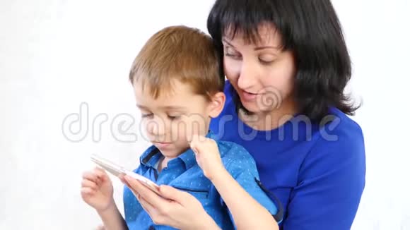 快乐的母亲和儿子用智能手机在白色背景下玩游戏微笑着玩得开心视频的预览图