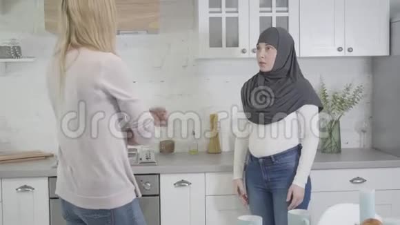 镜头接近穆斯林妇女戴头巾与金发白种人朋友在家争吵两个女人在室内争吵视频的预览图