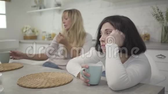 白种人成年女性的特写镜头她端着咖啡杯坐在桌旁她的金发女朋友喝着热辣视频的预览图