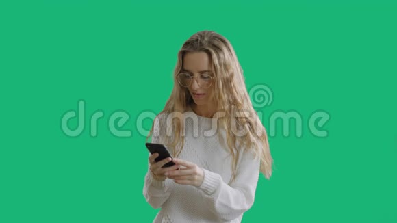 一个戴着眼镜的快乐美丽女孩的画像正看着一部手机用绿色屏幕的色度键庆祝视频的预览图