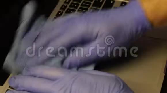 一个戴橡胶手套的人正在清洗他的笔记本电脑他用餐巾擦手提电脑键盘保护工作设备免受视频的预览图