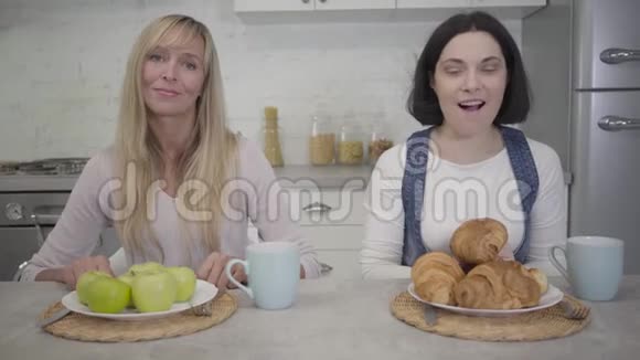 两个白人妇女坐在餐桌前吃食物的肖像有苹果的盘子站在金发女人和视频的预览图