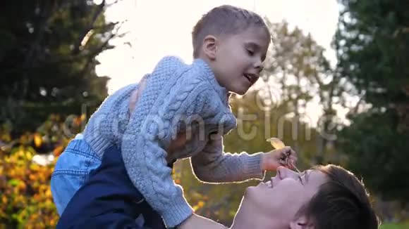 一个年轻的父亲和一个孩子玩把他抱在怀里吐了出来太阳阳光透过孩子笑声视频的预览图