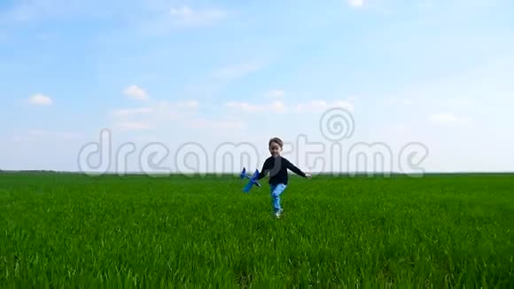 一个快乐的小男孩手里拿着一架玩具飞机在蓝天的映衬下穿过一片绿色的田野或草地孩子视频的预览图