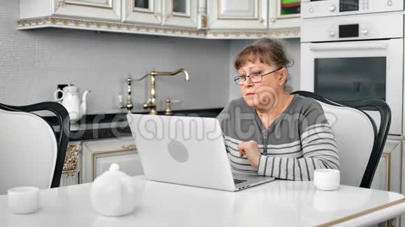 戴眼镜的白发苍苍的老太太在网上购物看着笔记本电脑屏幕视频的预览图
