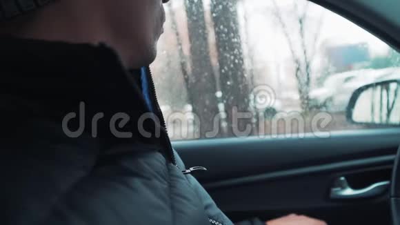 白人年轻人坐在车里打开窗户街上下雨了特写视频的预览图