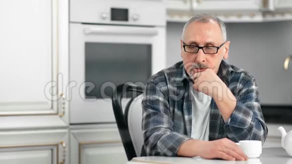 咖啡休息时坐在白色厨房的浅灰色头发休闲老人的画像视频的预览图
