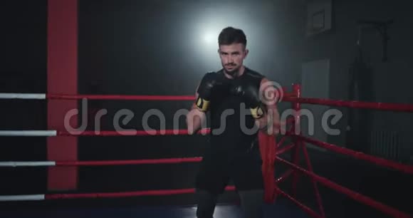 拳击手在镜头前在拳击场中间的一个黑暗的体育课上视频的预览图
