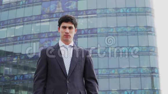 穿着商务套装和领带的白人帅哥站在一栋带有全景窗户的高层建筑的背景下视频的预览图