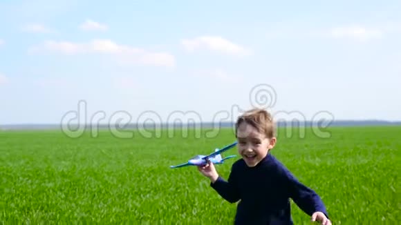 一个快乐的笑的男孩跑过一个绿色的田野与蓝天手里拿着一架玩具飞机孩子视频的预览图