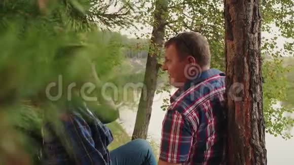 成年夫妇在针叶林的河岸上快乐的男人和女人在松林地的河岸上放松视频的预览图