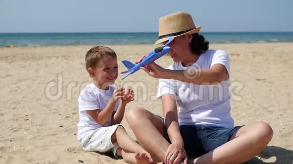 幸福的家庭一位母亲和她的儿子正坐在阳光明媚的夏日沙滩上玩玩具飞机视频的预览图