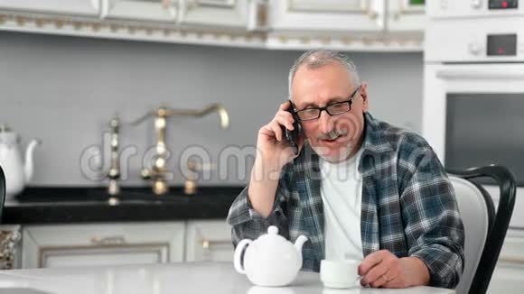 嘲笑老年男性在厨房用智能手机喝茶视频的预览图
