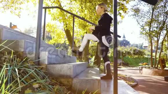 穿着运动服的金发女郎在公园的混凝土楼梯上伸展视频的预览图