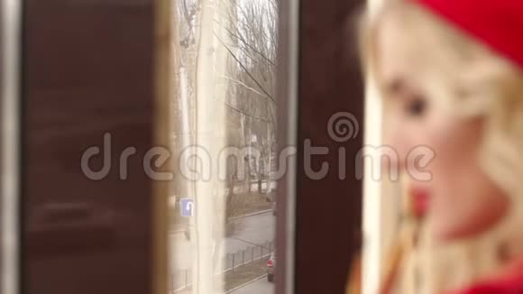 一个穿着红色连衣裙和一顶红色帽子的妆容鲜艳的女孩站在窗户附近视频的预览图