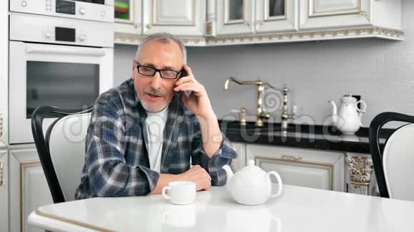 热情的英俊胡子爷爷在豪华的白色厨房里用智能手机聊天视频的预览图