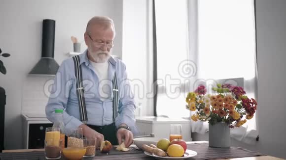 戴眼镜爱吃适当营养的老带胡子的人准备健康的水果沙拉饮料维生素汁视频的预览图